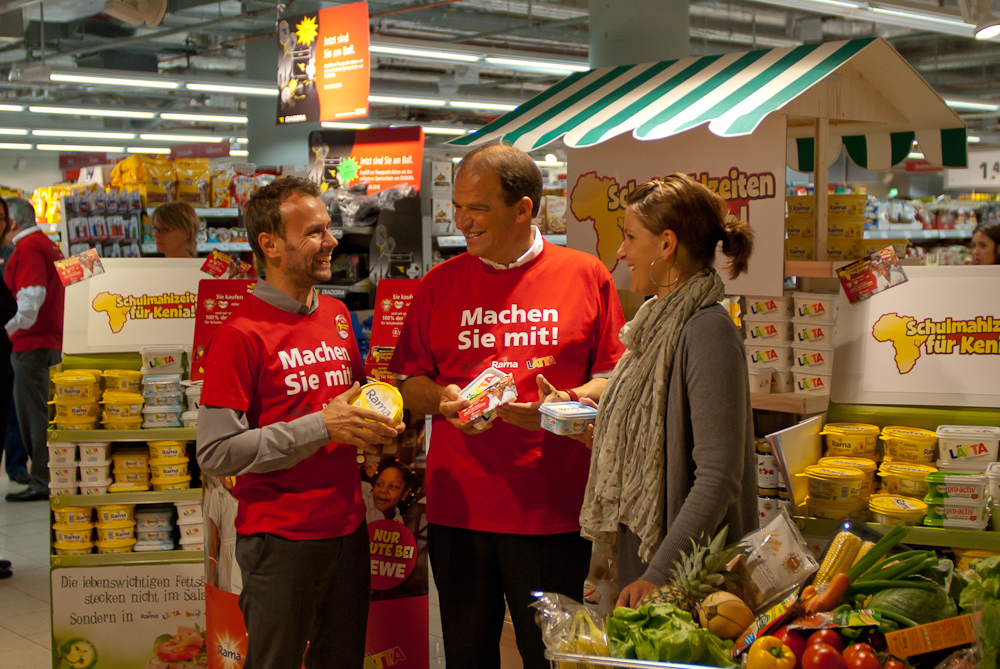 Ralf Südhoff vom WFP und Harry Brouwer von Unilever machen einer Musterkäuferin das WFP-Programm und Rama schmackhaft